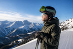 Skier in a black helmet and mirrored sunglasses standing on a groomed slope above a mountain range